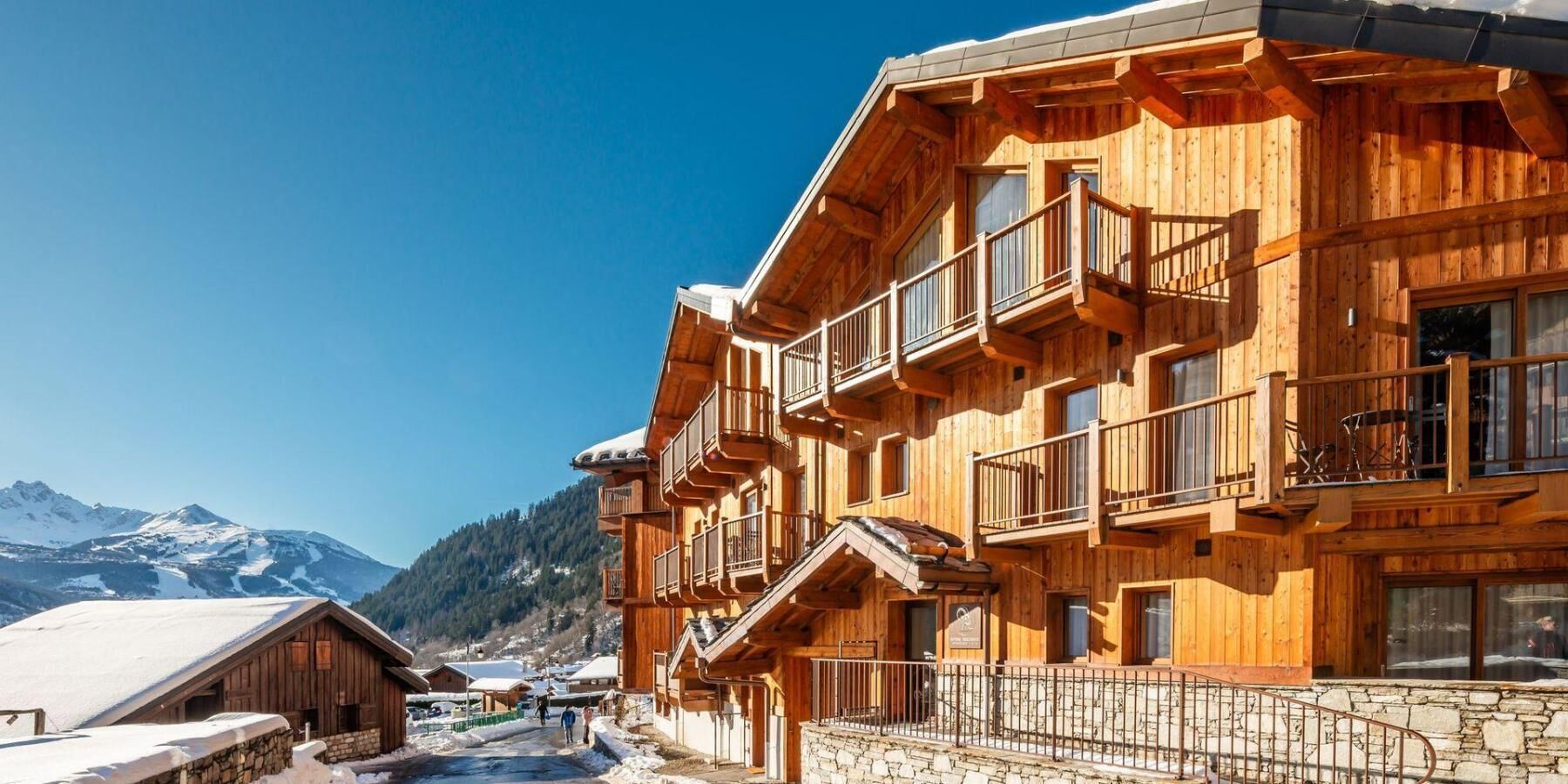 Un chalet in legno con balconi, un sentiero in pietra e montagne sullo sfondo.