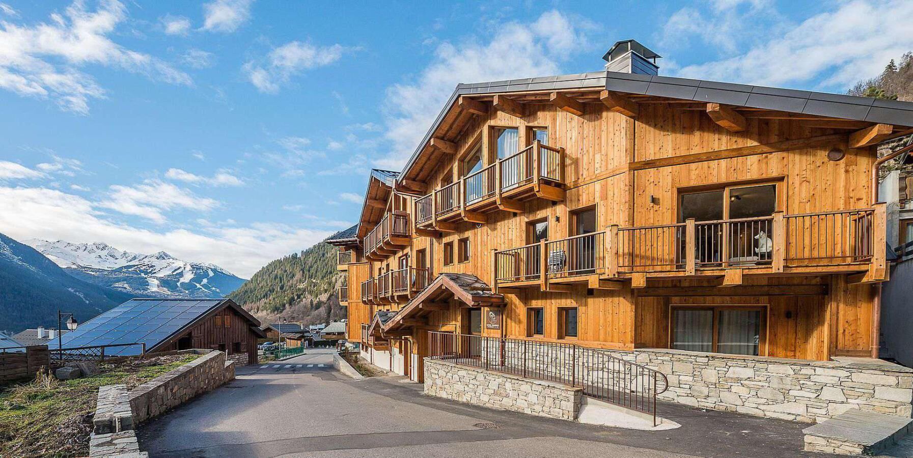 A wooden multi-story building with balconies, a stone pathway, and a mountainous backdrop.