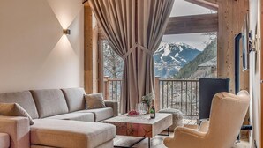 A cozy living room with a sofa, armchair, and coffee table. A window offers a view of snow-capped mountains. - 1st floor, swimming pool, sauna, balcony, fireplace or stove, parking, tv, ski locker, 83m² (Champagny-en-Vanoise)