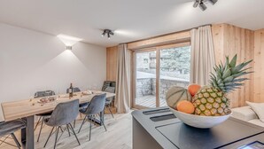 Ett modernt matområde med ett träbord, stolar och en skål med frukt på en bänkskiva.