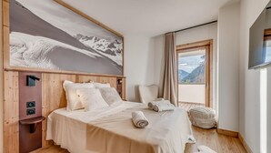 Un dormitorio con una cama grande, cabecera de madera, televisor montado y vistas a la montaña.