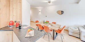 Een moderne keuken met een eethoek, met een houten wand, een marmeren aanrechtblad en oranje stoelen.