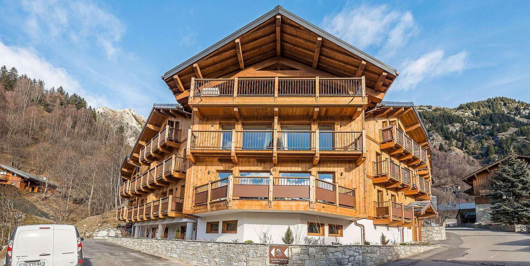A multi-story wooden building with balconies, a stone foundation, and a mountainous backdrop.