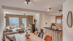 A modern living room with a wooden dining table, a sofa, and a kitchen area with a built-in oven and a bar counter. - 1st floor, swimming pool, sauna, balcony, fireplace or stove, parking, tv, ski locker, 71m² (Champagny-en-Vanoise)