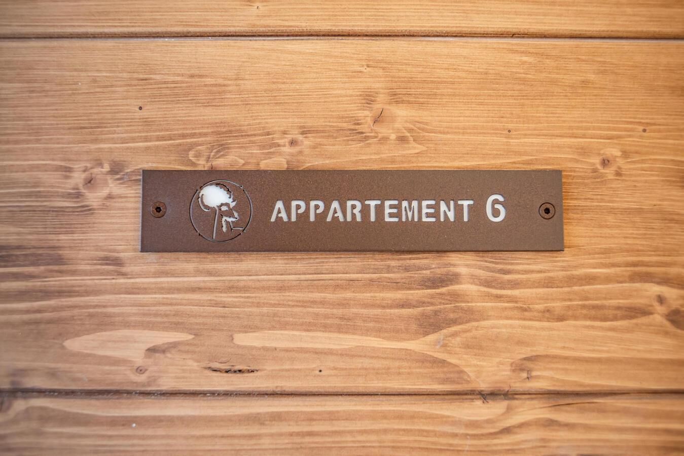 Un pannello di legno con la scritta 'APPARTMENT 6' e un simbolo di buca per chiave.