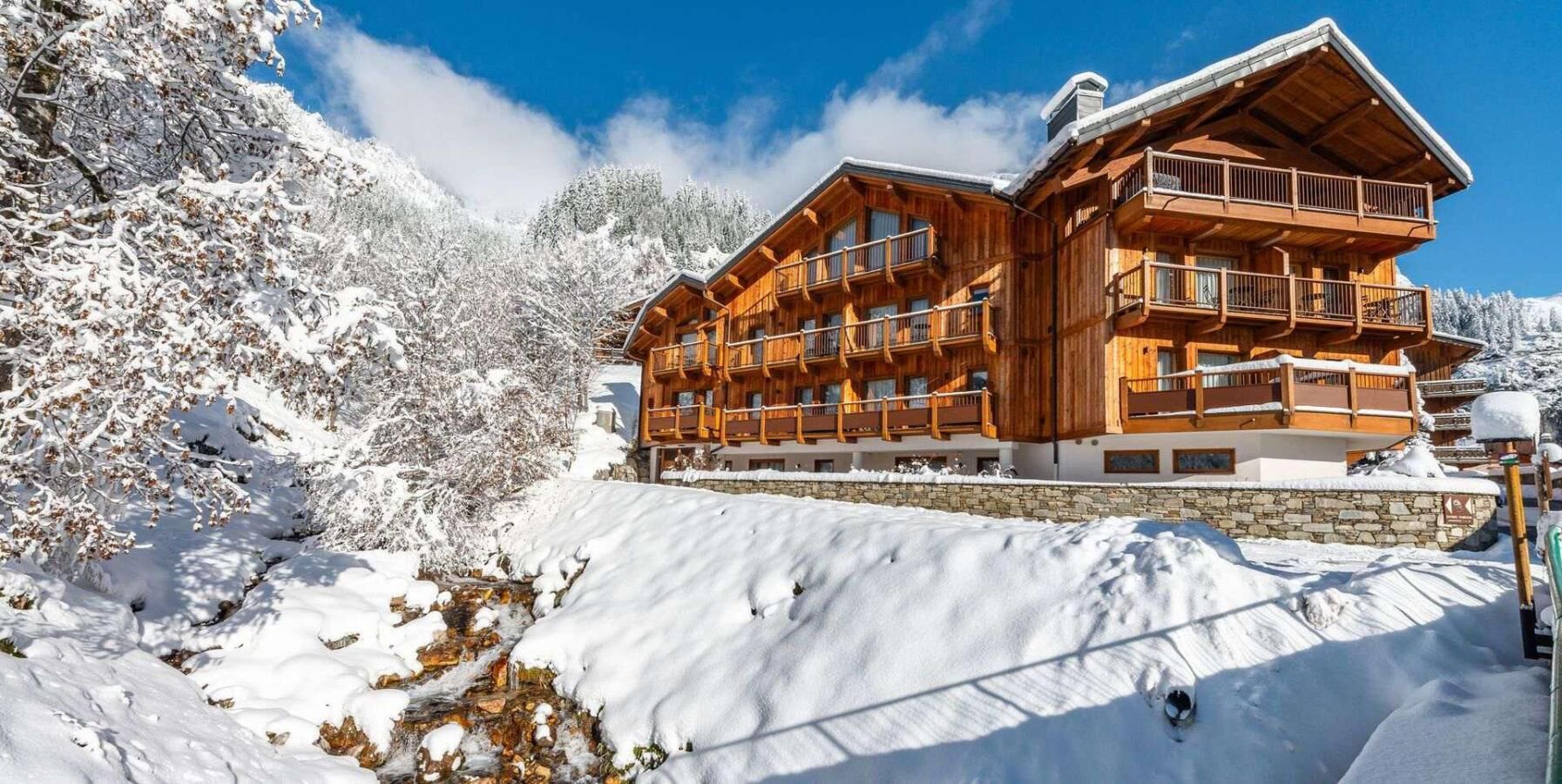 Una cabaña de madera con varios balcones, rodeada de árboles cubiertos de nieve y un cielo despejado.
