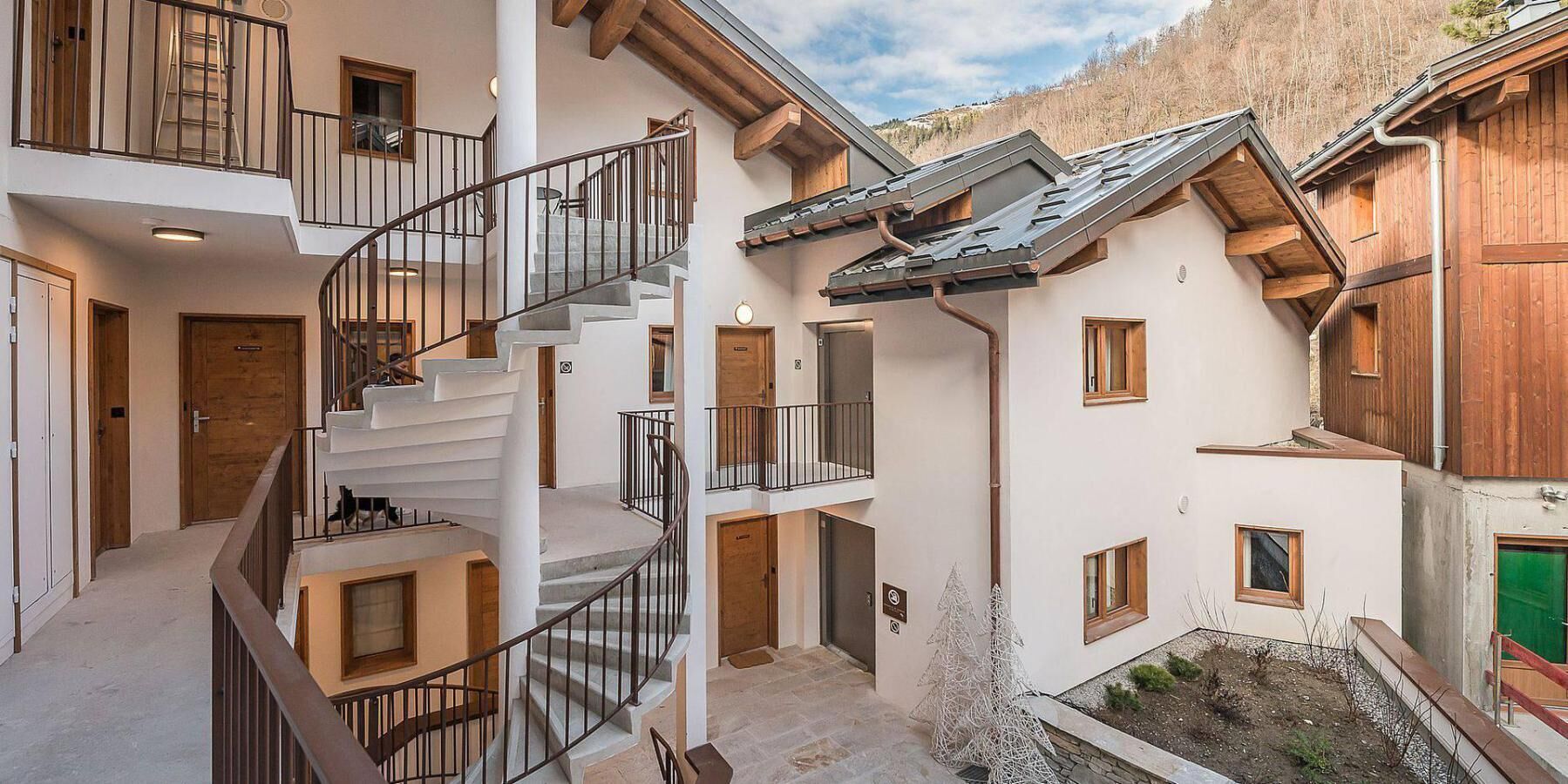 A multi-level building with a central spiral staircase, multiple balconies, and a view of a mountainous landscape.