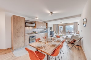 A modern kitchen with wooden cabinets, a dining area with orange chairs, and a view of a balcony.