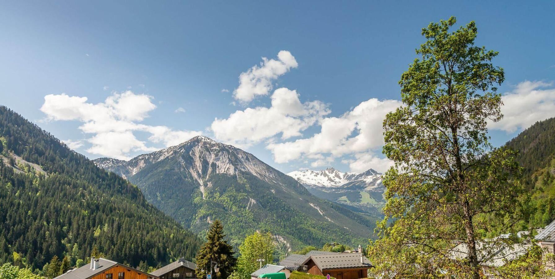 Paisagem montanhosa com um pico proeminente, uma cabana pequena e uma árvore em primeiro plano.