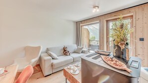 A modern living room with a sofa, a chair, a coffee table, and a kitchen area with a stove and a decorative plant. - Ground floor, swimming pool, sauna, balcony, fireplace or stove, parking, tv, ski locker, 59m² (Champagny-en-Vanoise)