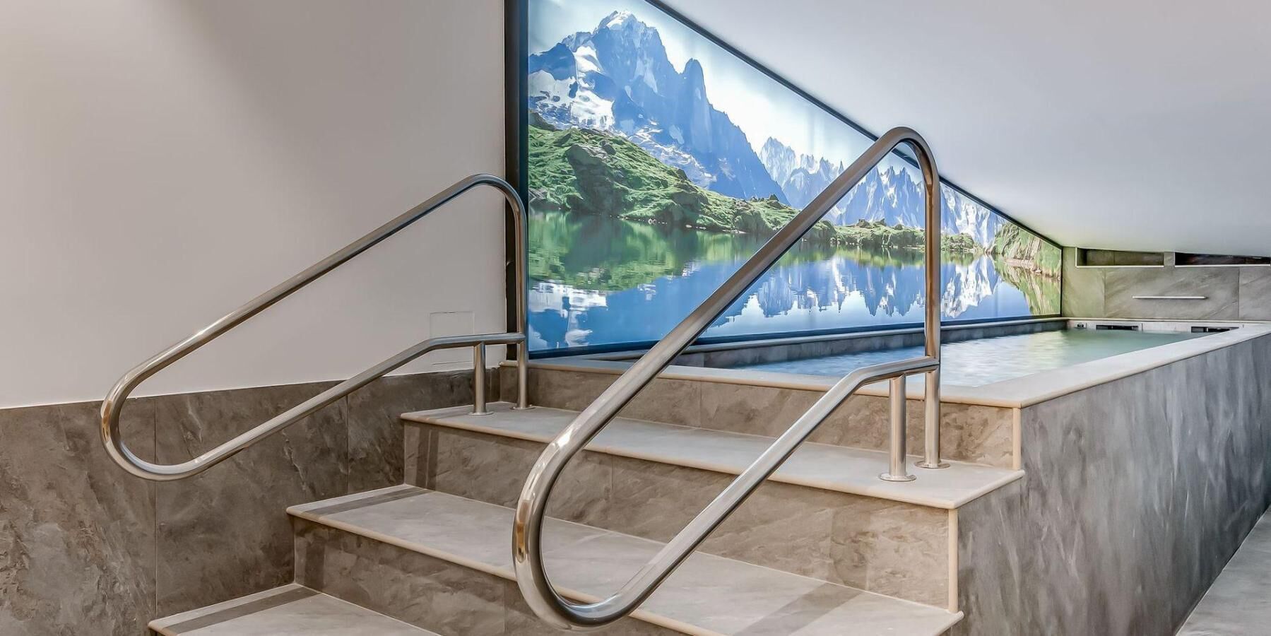 Un escalier moderne avec des rampes en métal, menant à un espace piscine doté d’une grande fenêtre donnant sur un paysage montagneux.