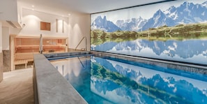 Une piscine intérieure moderne offrant une vue dégagée sur un paysage montagneux qui se reflète dans l’eau.