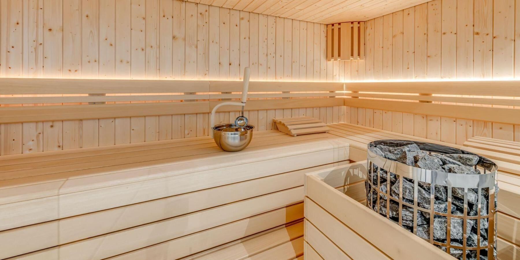 Una sauna con pareti e panche in legno, una bacinella metallica e un contenitore riempito di pietre.