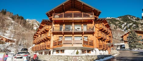 A multi-story wooden chalet with balconies, a stone foundation, and a ski resort setting.