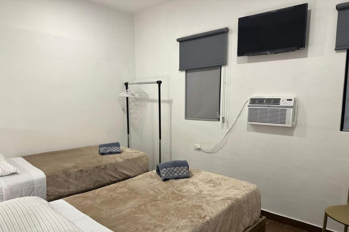 Una habitació d'hotel amb dos llits, televisió, aire condicionat i una finestra amb estore.