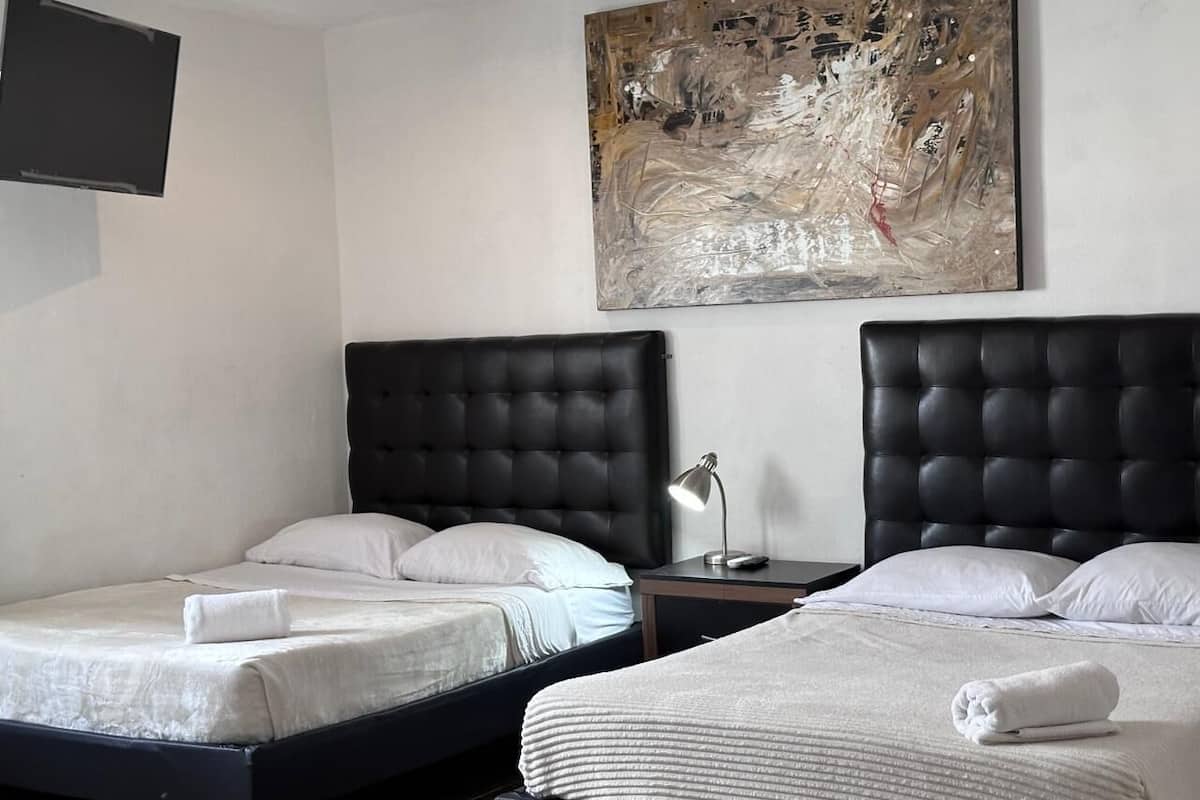 Habitació d'hotel amb dos llits, televisió de pantalla plana i un gran quadre abstracte a la paret.