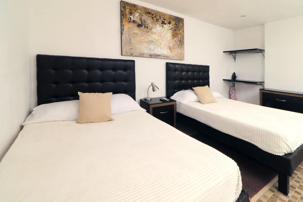 Una habitació d'hotel amb dos llits, cadascun amb un capçaler negre, roba de llit blanca i un coixí beix. Hi ha un quadre a la paret sobre els llits, una taula petita amb una làmpada i una estant amb una tovallola plegada.