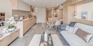 Een moderne keuken met houten kasten, een eethoek met een tafel voor vier personen, en een gezellige woonkamer met een bank en decoratieve kussens.