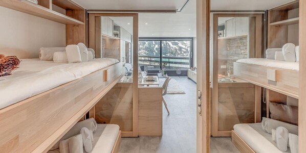 A modern, multi-level bedroom with bunk beds, a dining area, and a view of a snowy landscape.