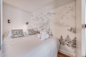 A bedroom with a bed, pillows, a wall mural, and two wall-mounted lights.