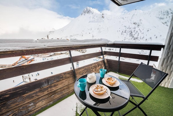 A balcony with a table, chairs, and a view of a snowy mountain and ski resort.
