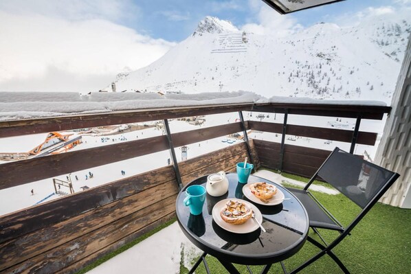 A balcony with a table, chairs, and a view of a snowy mountain and ski resort.