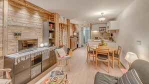 Een moderne woonkamer met een open haard, een eethoek met een houten tafel en stoelen, en een keuken met witte kasten en een magnetron.