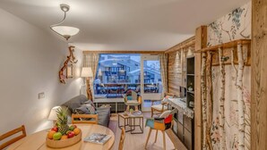 Een moderne woonkamer met een bank, eettafel en stoelen, een uitzicht op een gebouw door een glazen deur, en houten decoratie.