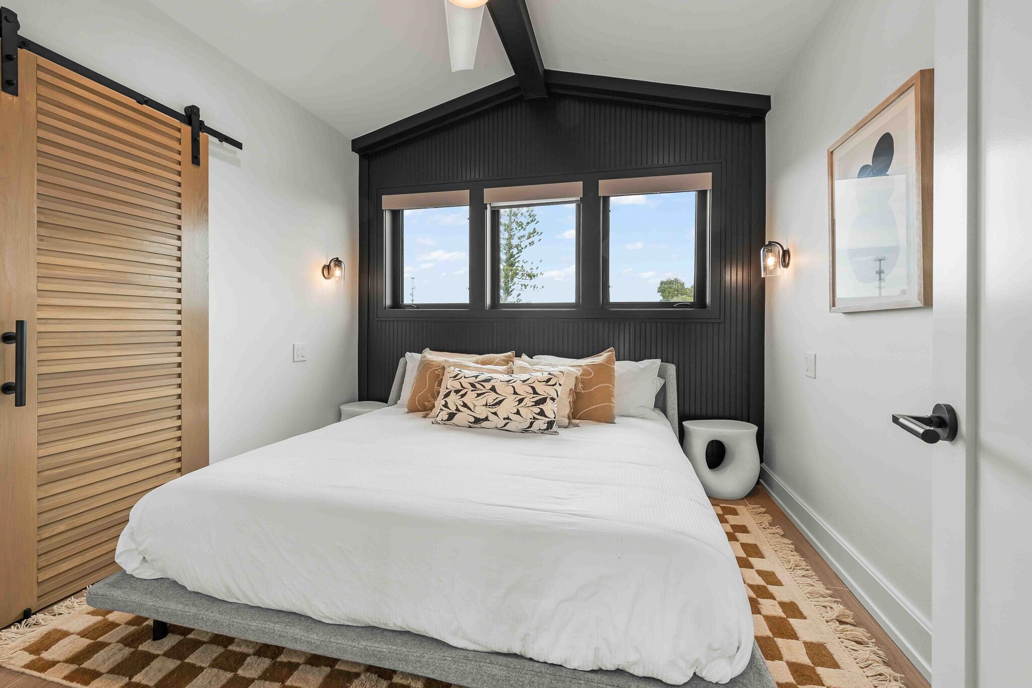 A bedroom with a bed, a window, a door, and a wall-mounted light fixture.
