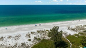 En strand med klart turkis vand, hvidt sand og sparsom vegetation.