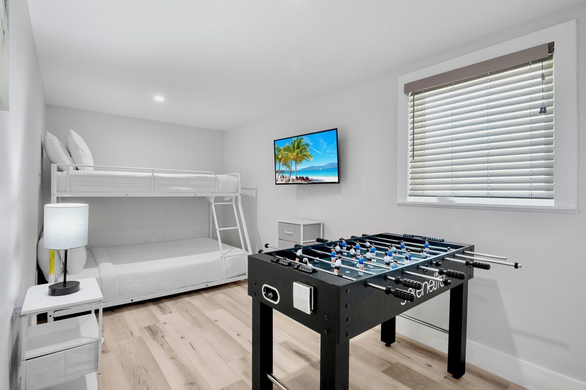 Une chambre moderne équipée d’un lit superposé, d’un baby-foot, d’une télévision et d’une fenêtre avec des stores.