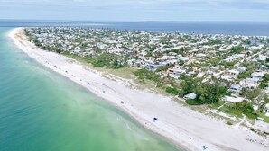 Vue aérienne d’une ville côtière avec une longue plage de sable, une zone résidentielle densément peuplée et des eaux bleues et limpides.