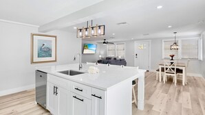 Une cuisine moderne avec des meubles blancs, un grand îlot central et un coin repas comprenant une table et des chaises.