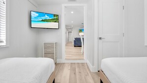 Une chambre d’hôtel avec deux lits, un téléviseur fixé au mur, un plancher en bois et une vue sur le couloir.
