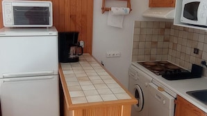 Een kleine keuken met een koelkast, wasmachine, magnetron en houten kastjes.