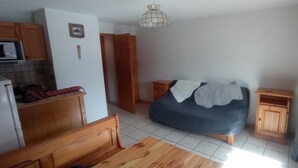 Een compacte slaapkamer met een bed, houten nachtkastjes, een kledingkast en een kitchenette.