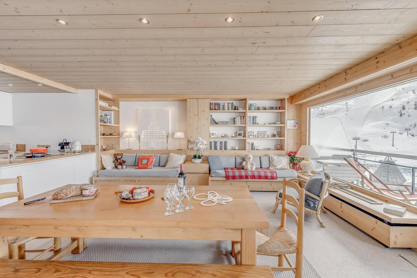 Ein gemütliches Blockhaus-Interieur mit Essbereich, einer Couch, einem Bücherregal und Blick auf eine verschneite Landschaft.