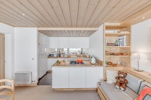 A modern kitchen with white cabinets, a wooden countertop, and a central island. There is a bookshelf with books and decorative items, and a teddy bear on a grey sofa. - 20m from resort center, 5th floor, view mountain, tv, ski locker, 80m², Tignes (Tignes)