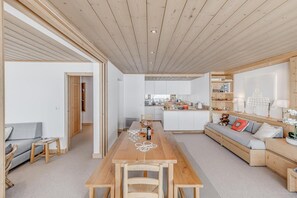 A modern interior with a wooden dining table, grey sofa, and a kitchen area. - 20m from resort center, 5th floor, view mountain, tv, ski locker, 80m², Tignes (Tignes)