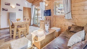 Ein gemütliches Blockhauss-Interieur mit einem Holzesstisch, Stühlen, einer Couch und einem an der Wand befestigten Fernseher.