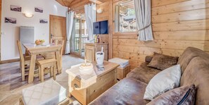 A cozy cabin interior with a wooden dining table, chairs, a sofa, and a TV mounted on the wall.