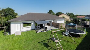 Una casa residencial con un porche cubierto, un trampolín y un conjunto de columpios de madera.