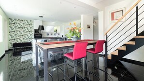 Una cocina moderna con una isla central, un comedor con sillas rojas y una escalera.
