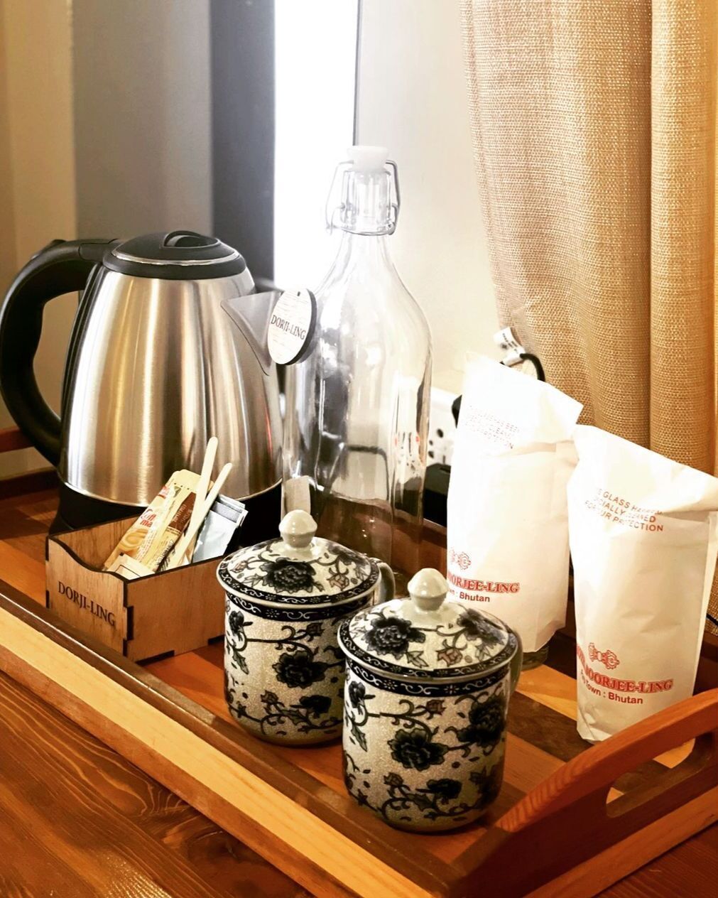 A tray with a stainless steel coffee pot, a glass bottle, two ceramic containers with lids, a box labeled 'DORJI-LING', and two white paper bags with 'DORJI-LING' branding.
