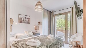 Un dormitorio moderno con una cama grande, una lámpara colgante, un cuadro y vistas al exterior a través de una puerta corrediza.
