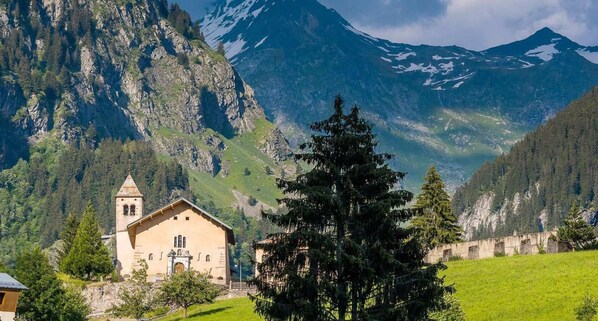 A mountain church with a bell tower, surrounded by lush greenery and steep cliffs.