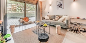 A modern living room with a sofa, coffee table, and a chair. There is a large window with a view of a village.
