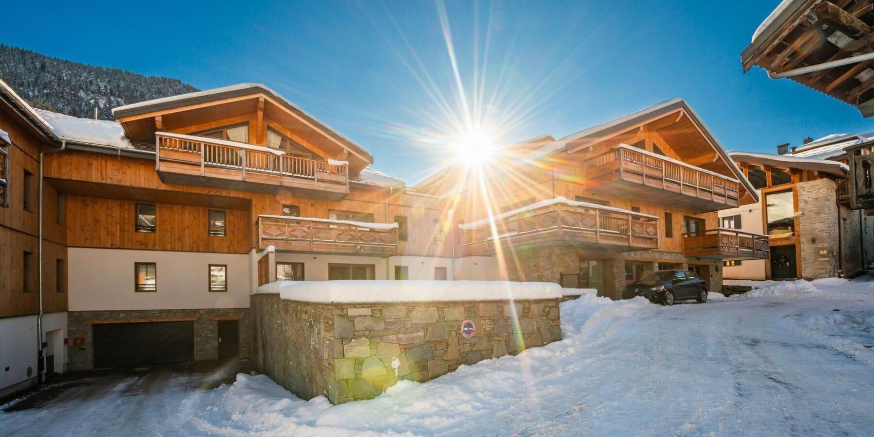 Ein mehrstöckiges Holzhaus mit Balkonen, einem Steinkamin und einem mit Schnee bedeckten Gelände.