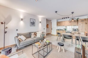 A modern apartment with a grey sofa, a dining area, and a kitchen with wooden cabinets.