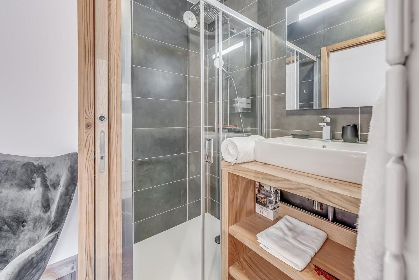 Un bagno moderno con cabina doccia in vetro, mobile bagno in legno con lavandino e specchio soprastante.
